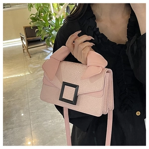 Detail of light pink faux snakeskin handbag with black buckle and bow on the handle