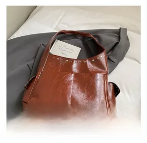 Detail view of brown glossy faux leather shoulder bag featuring metal rivet studs