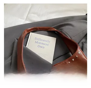 Close-up of retro brown glossy leather shoulder bag with silver rivet details on grey fabric