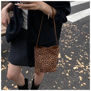 Close-up of leopard print bucket bag with brown shoulder strap worn by a model outdoors