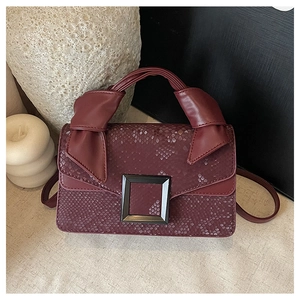 Close-up of burgundy embossed snakeskin handbag with matte square buckle and knotted handle