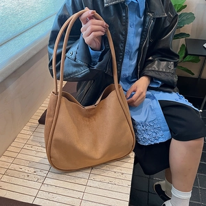 Detail of a large brown suede tote bag with soft texture shown on model's shoulder