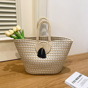 Handwoven beige and black striped tote bag with tassel and logo on wooden surface