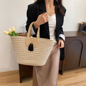 Fashion woven straw tote bag with round handles and tassel, shown on model for autumn 2025