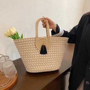 Striped woven handbag with black tassel and flowers on a dark wooden table