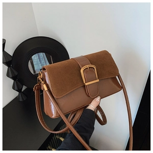 Brown leather and suede shoulder bag with gold metal buckle shown in a modern studio setting