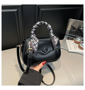Detail of black square handbag featuring decorative heart silk scarf and wave-flap design