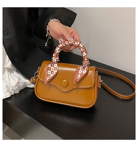 Detail of caramel leather handbag featuring silk scarf handle and adjustable shoulder strap
