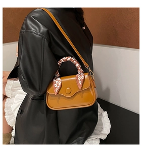 Detail of crossbody bag with decorative scarf on handle and round metal buckle