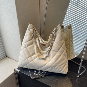 Quilted beige large tote bag with chain strap and twist lock on a minimalist surface