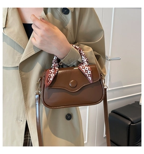 Detail of dark brown square crossbody bag with scalloped flap and heart silk scarf handle