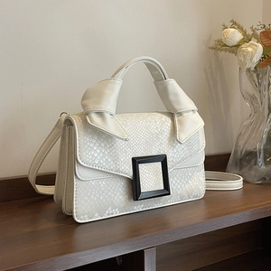Chic white snake-print trapezoid handbag with black buckle on elegant wooden shelf