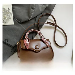 Detail of a brown leather crossbody bag with a decorative heart-patterned silk handle scarf