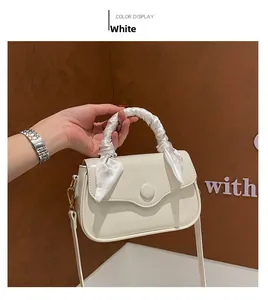 Detail of white leather handbag featuring a silk scarf-wrapped handle and gold hardware