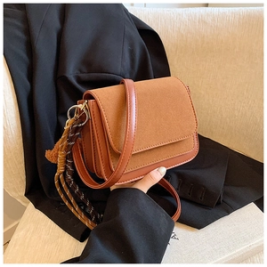 Detail view of a vintage brown crossbody square bag with suede flap and braided charm