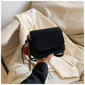 Detail of black square bag featuring suede flap and woven charm with brown pompom