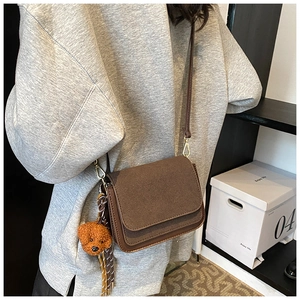 Detail of dark brown square crossbody bag with suede texture and plush puppy charm