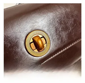 Macro shot of retro bronze rotating lock on dark brown oil wax leather shoulder bag