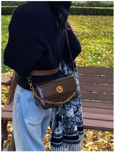 Detail of dark brown leather crossbody bag with gold chain strap on autumn background