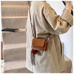 Detail of brown flap crossbody bag with plush bear charm and leather strap on model