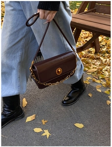 Close-up of wine red patent leather shoulder bag with golden chain and metal turn-lock