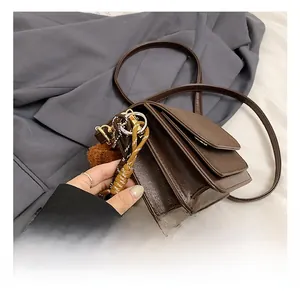 Detail view of multi-layer dark brown square bag with gold ring and plush ball charm