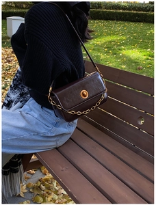 Detail of vintage brown leather crossbody bag with gold chain strap in outdoor setting