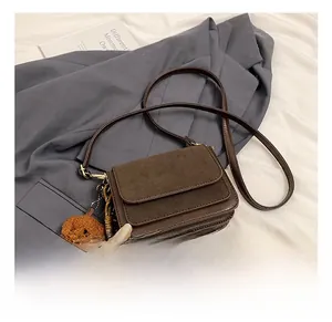 Detail of square brown crossbody bag with matte flap and cute teddy bear pendant charm