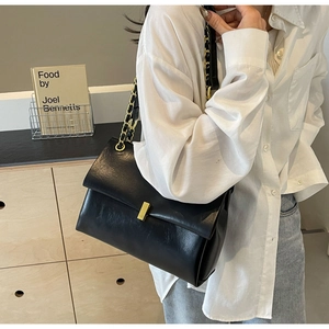 Dettaglio di una borsa a tracolla nera vintage con fibbia dorata e tracolla a catena