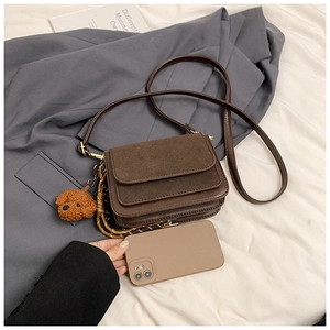 Detail of dark brown leather crossbody bag with accordion structure and teddy charm