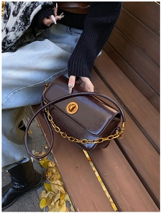 Close-up of vintage dark brown leather handbag with gold chain and metal lock on wooden bench