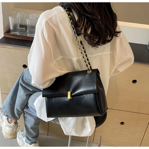 Detail of black crossbody bag featuring a golden metallic lock and elegant chain strap