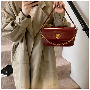 Detail of burgundy glossy leather square bag with gold chain and round clasp on a trench coat