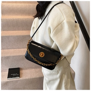 Detail view of a black glossy leather shoulder bag featuring a gold chain and turn-lock closure
