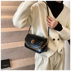 Close-up of black glossy shoulder bag with chunky gold chain strap and metal clasp detail