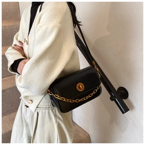 Detail of matte black square bag featuring a gold chain strap and rotary lock
