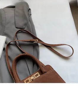 Detail of adjustable strap with gold buckle on brown matte leather handbag