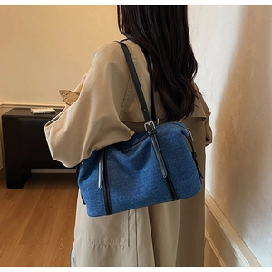 Detail of blue denim shoulder bag with black leather strap and silver buckle in cozy room