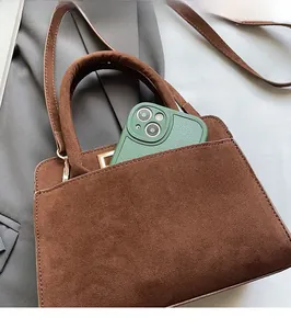 Detail of brown suede handbag featuring a functional front pocket for smartphone storage