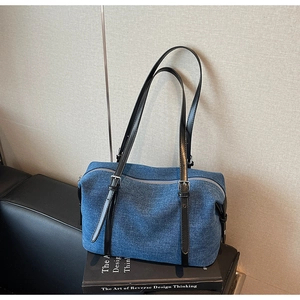 Detail of dark blue denim underarm bag featuring black leather strap and silver zipper