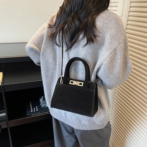 Lifestyle shot of black matte leather handbag with silver twist lock on a shoulder