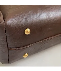 Dettaglio della base della borsa in pelle marrone con piedini in metallo dorato e cuciture