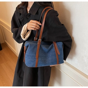 Close-up of denim shoulder bag with brown leather straps and silver metal hardware details