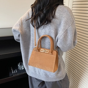 Brown suede handbag with metal twist lock shown in a casual lifestyle setting