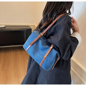 Detail of blue denim shoulder bag showing texture and brown leather strap with silver buckle