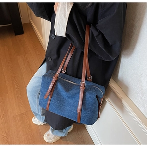 Detail of blue denim shoulder bag featuring brown leather straps and metal buckles