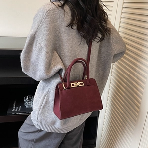Detail of burgundy frosted leather handbag with gold metal lock and long shoulder strap