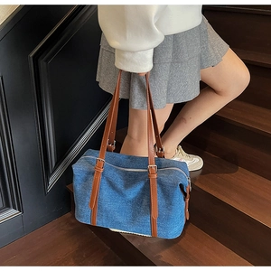 Detail of blue denim shoulder bag with brown leather handles and silver zipper closure