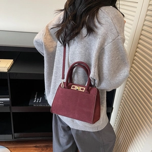Detail of burgundy matte suede handbag featuring golden twist lock and twin top handles