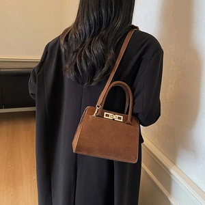 Brown matte suede handbag worn by model with adjustable strap and metal lock detail
